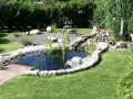 Ein idyllischer kleiner gartenteich ideen mit Steinumrandung, Holzsteg und üppiger Bepflanzung.