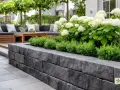 Moderne Terrasse mit Steinmauer und einem üppigen Beet. Ein gemütliches Lounge-Set lädt zum Entspannen ein.