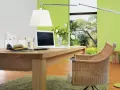 Ein Schreibtisch aus Nussbaumholz mit Laptop und Stoffmustern. Grüne Wand und Rattanstuhl. Welche Farbe passt zu Nussbaum? Grün und Beige.