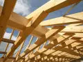 Holzkonstruktion eines Dachstuhls im Bau, mit sichtbaren Balken und Streben. Das Sprengwerk des Dachstuhls wird durch das Sonnenlicht beleuchtet.