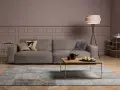 Ein taupefarbenes Sofa mit Kissen und ein Couchtisch mit Obst. Die Wandfarbe ist ein warmes Braun, das zeigt, welche Farbe passt zu Taupe.