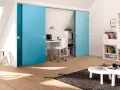 Ein kleines Arbeitszimmer einrichten: Blaue Schiebetüren verbergen einen Schreibtisch mit Laptop und Bürostuhl. Bücherregale und ein Couchtisch ergänzen den Raum.