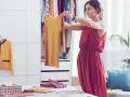 Frau sortiert Kleidung nach der Marie Kondo Methode. Ein gelbes Oberteil wird in die Hand genommen, daneben ein gelber Blazer und ein Korb mit gefalteten Textilien.