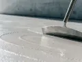 Glatter, nasser Beton wird mit einem Werkzeug bearbeitet, um die Oberfläche für das Beton ausschalen vorzubereiten.