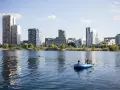 Zwei Männer treiben in einem Schlauchboot auf dem See der Seestadt Aspern. Im Hintergrund ragt die moderne Architektur der Stadt auf.