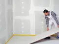 Handwerker verlegt eine Platte für einen Trockenestrich. Verschiedene Estrich Arten sind für unterschiedliche Bauvorhaben geeignet.