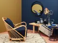 Ein Rattansessel mit dunkelblauem Kissen steht auf einem Teppich. Welche Farbe passt zu Gold? Das goldene Spiegelbild an der Wand und die gelbe Wandfarbe harmonieren mit dem tiefen Blau.