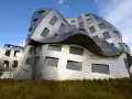 Ein futuristisches Gebäude mit geschwungenen Metallfassaden, typisch für Frank Gehry Bauwerke, ragt aus hohem Gras empor.