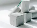 Betonwürfel und -zylinder in verschiedenen Formen, die die Vielfalt der **Beton festigkeitsklassen** symbolisieren. Ein grüner Stab ragt aus einem der Objekte.