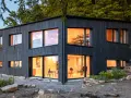 Modernes Haus mit Fassade im Shou Sugi Ban Stil. Große Fenster lassen warmes Licht herein.