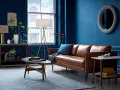 Ein Wohnzimmer mit braunem Ledersofa und blauen Wänden. Das Braun ist die perfekte gegenfarbe von braun, die dem Raum Tiefe verleiht.