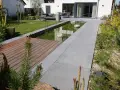 Moderner Vorgarten gestalten: Teich, Holzdeck und Sitzbereich laden zum Entspannen ein. Grüne Rasenflächen und blühende Pflanzen schaffen eine harmonische Atmosphäre.