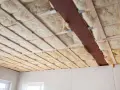 Decke mit Holzbalken und Dämmung. Hier sieht man, was ist Glaswolle: ein isolierendes Material, das in Hohlräume eingebracht wird.
