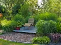 Entspannende Garten-Ideen: Eine Holzliege auf einer kleinen Terrasse inmitten üppiger Gräser und Pflanzen.