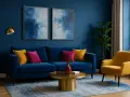 Ein Wohnzimmer mit dunkelblauen Wänden. Ein blauer Samtsofa mit gelben und pinken Kissen. Ein gelber Sessel. Welche Farbe passt zu dunkelblau? Gelb und Pink!