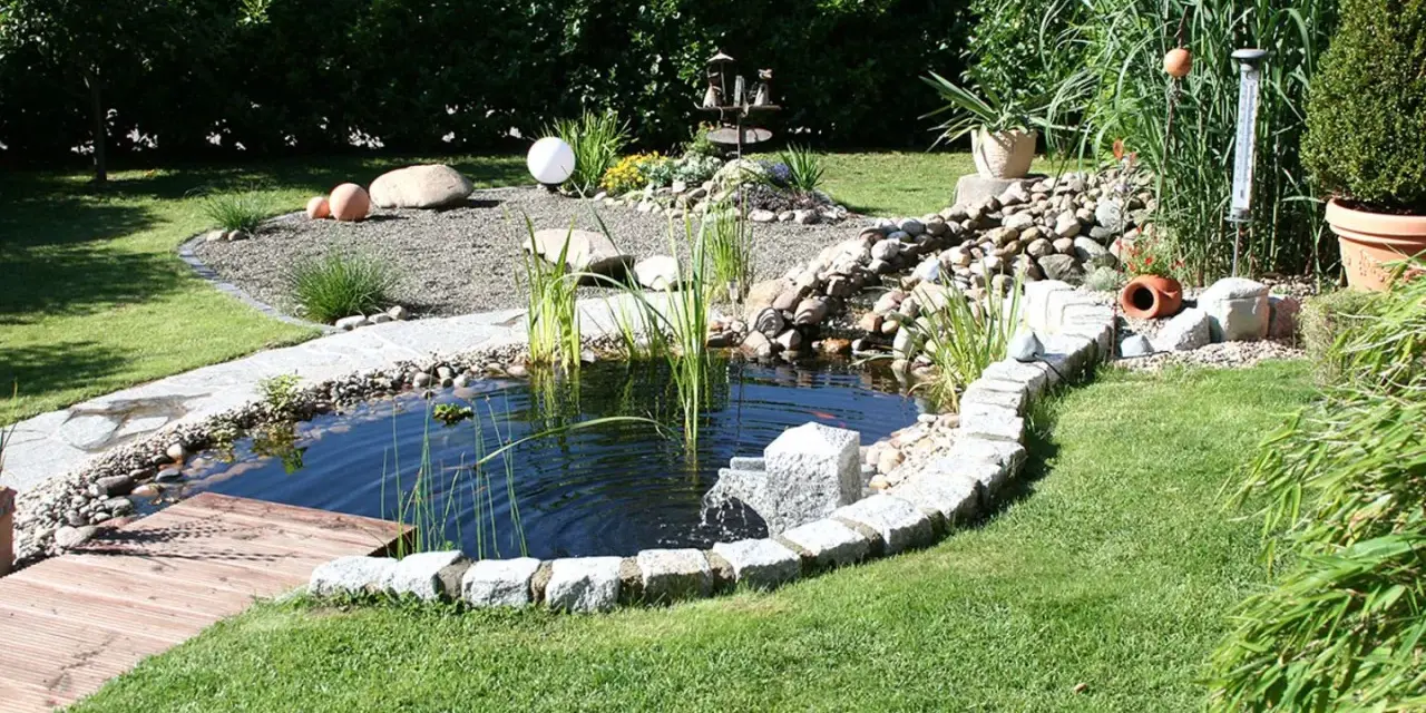 Ein idyllischer kleiner gartenteich ideen mit Steinumrandung, Holzsteg und üppiger Bepflanzung.