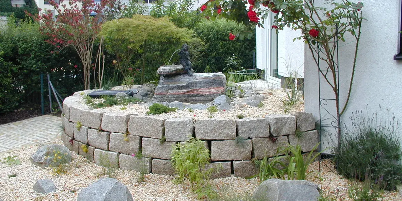 Moderner Hauseingang mit einem geschwungenen Steingarten und einem kleinen Wasserspiel. Ein Hingucker, der zeigt, wie man den Vorgarten modern gestalten kann.