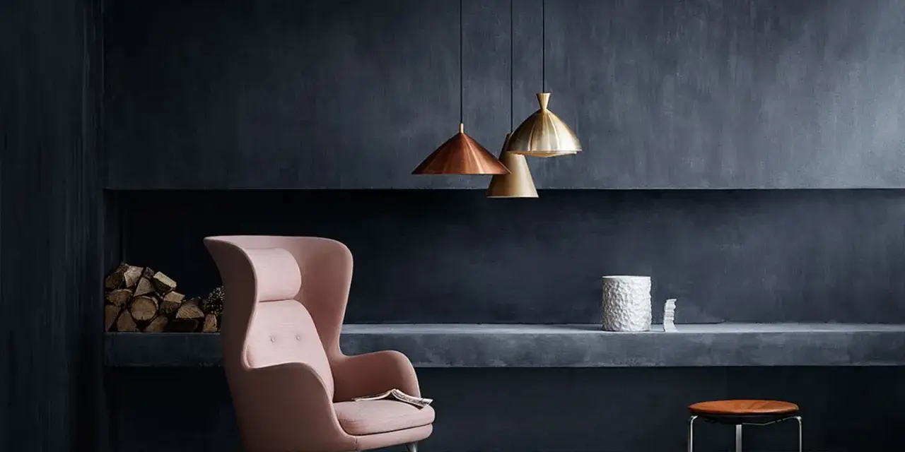 Ein rosafarbener Sessel vor einer anthrazitfarbenen Wand. Die Frage, welche Farbe passt zu Anthrazit, wird hier elegant beantwortet: Zarte Pastelltöne wie dieses Rosa schaffen einen stilvollen Kontrast.