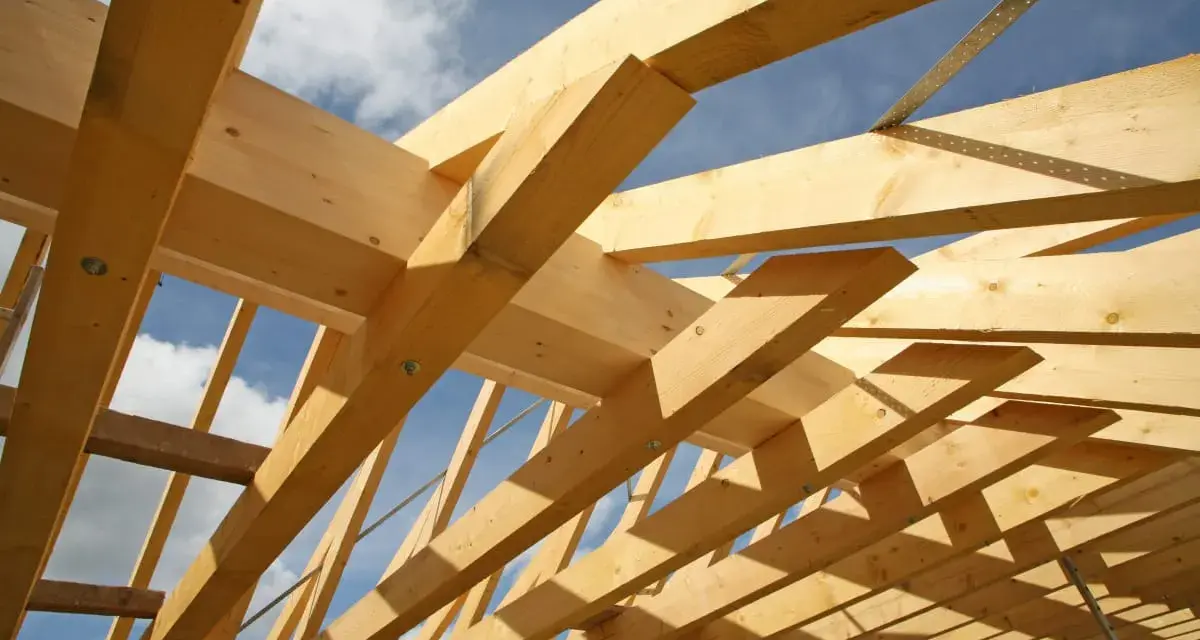 Holzkonstruktion eines Dachstuhls im Bau, mit sichtbaren Balken und Streben. Das Sprengwerk des Dachstuhls wird durch das Sonnenlicht beleuchtet.