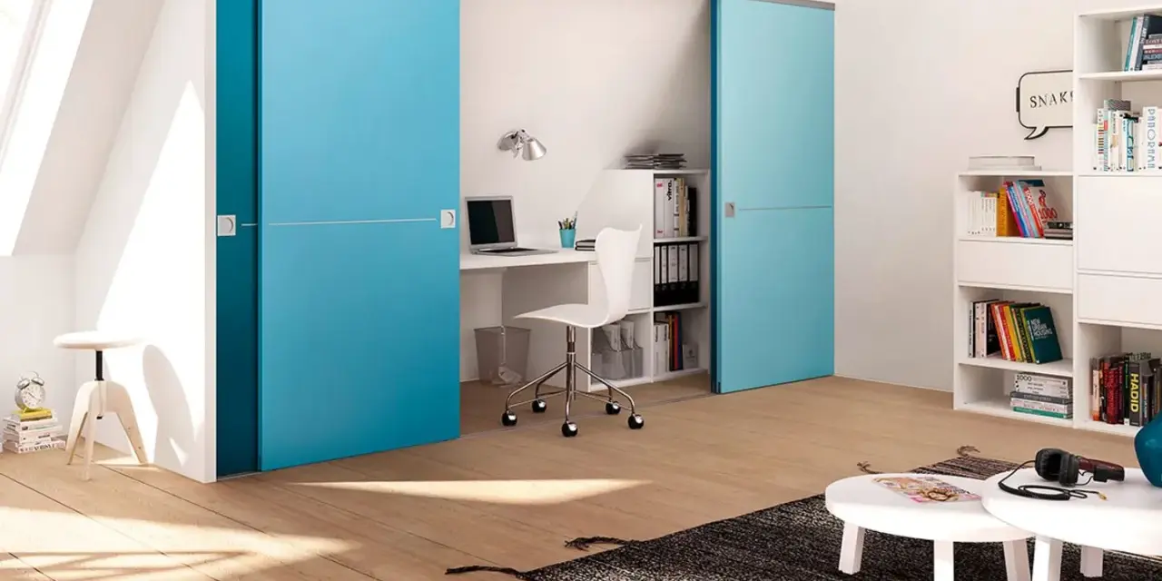 Ein kleines Arbeitszimmer einrichten: Blaue Schiebetüren verbergen einen Schreibtisch mit Laptop und Bürostuhl. Bücherregale und ein Couchtisch ergänzen den Raum.
