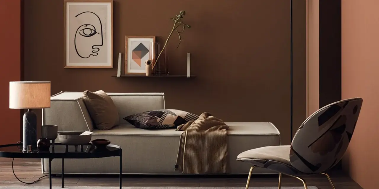 Gemütliches Wohnzimmer mit Sofa, Sessel und Tisch. Die Wände sind in warmen Brauntönen gehalten, die sich mit den Textilien und Dekorationen **braun mischen**.