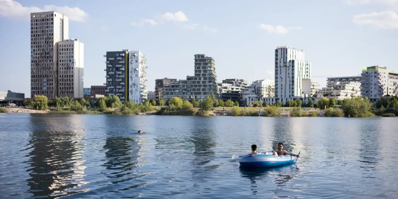 Zwei Männer treiben in einem Schlauchboot auf dem See der Seestadt Aspern. Im Hintergrund ragt die moderne Architektur der Stadt auf.