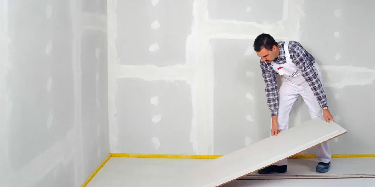 Handwerker verlegt eine Platte für einen Trockenestrich. Verschiedene Estrich Arten sind für unterschiedliche Bauvorhaben geeignet.