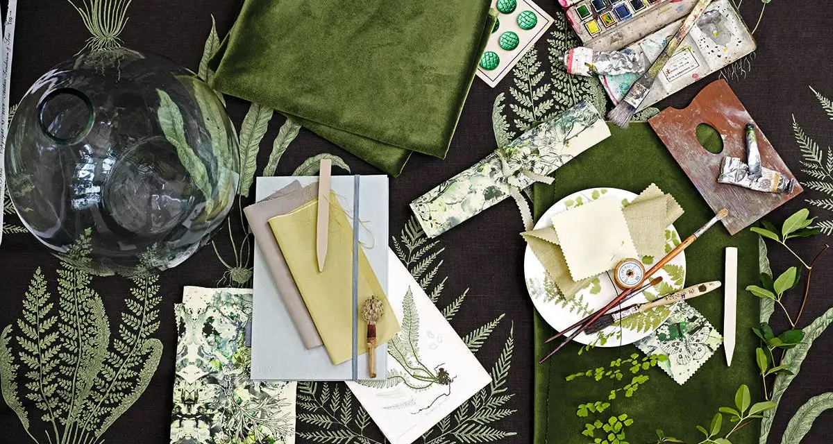 Ein Moodboard mit grünen Stoffen, Aquarellfarben, Pinseln und Farnmotiven. Hier wird gezeigt, was ein Moodboard ist: eine Sammlung von Inspirationen.