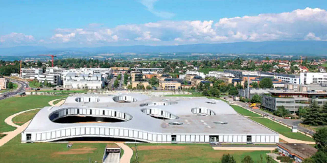 Das Rolex Learning Center in Lausanne, ein futuristisches Gebäude mit runden Öffnungen im Dach, umgeben von grünen Flächen und moderner Architektur.