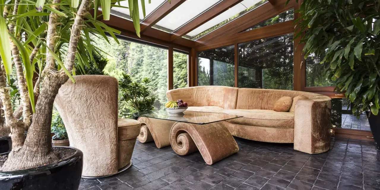 Gemütlicher Wintergarten mit bequemer Couch und Glascouchtisch. Pflanzen und viel Licht schaffen eine entspannte Atmosphäre, ideal zum Wintergarten einrichten.