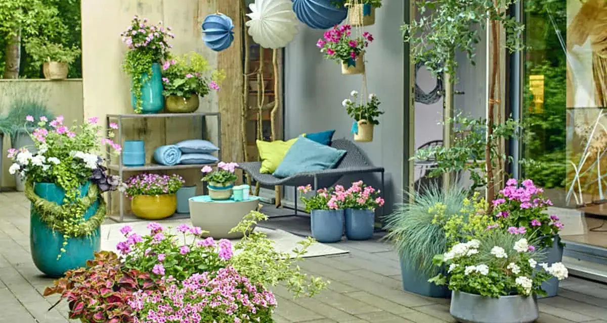 Bunte Blumen und grüne Pflanzen auf einer Terrasse, mit Hängekörben und Kissen. Tolle gartendeko ideen für Ihr Zuhause.