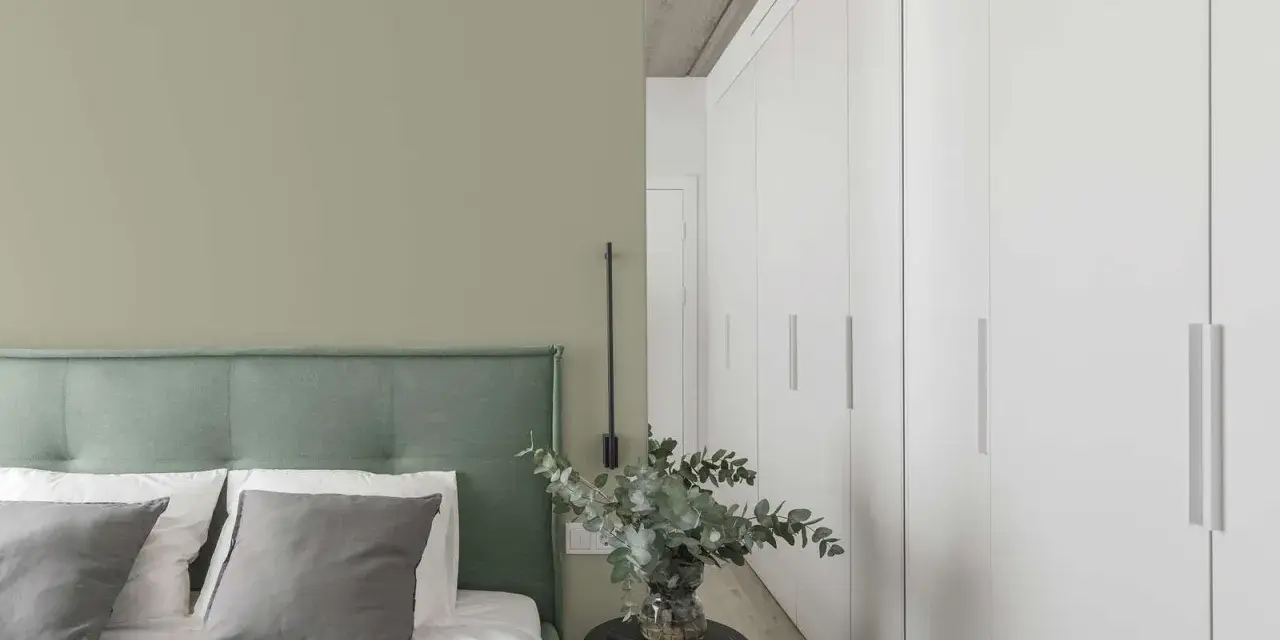 Ein Schlafzimmer mit einer Wand in hellem Olivgrün und einem Bett mit grünem Kopfteil. Der Unterschied zwischen Khaki und Oliv ist hier subtil, aber präsent.