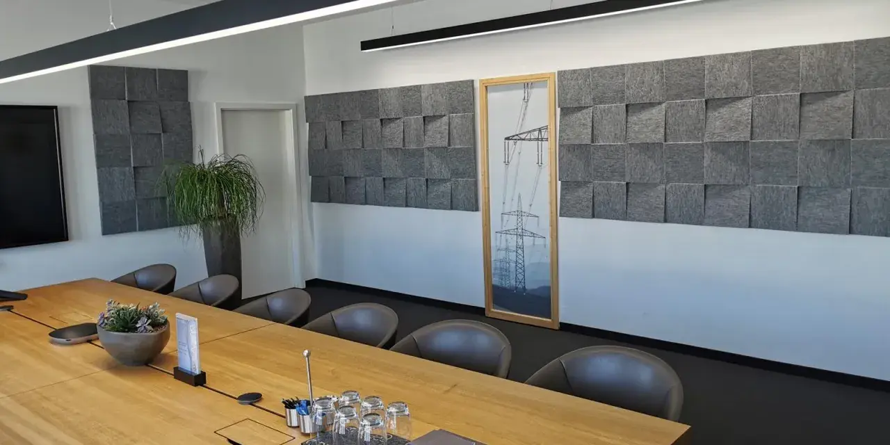 Moderne Konferenzraumgestaltung mit Akustikpaneelen an der Wand, um den **Schall im Raum zu reduzieren**. Ein großer Holztisch mit Gläsern und Notizbüchern steht im Vordergrund.