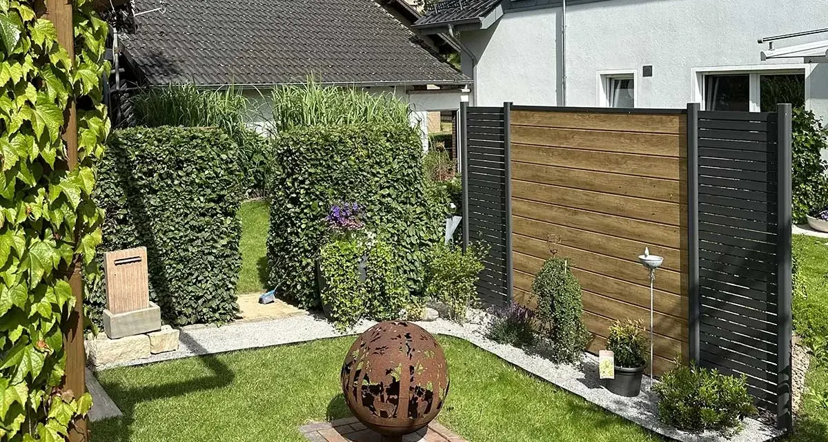 Schöner Garten mit Hecken und Holzzaun als Sichtschutz. Eine Feuerkugel und Pflanzen schaffen Gemütlichkeit. Tolle Ideen für Sichtschutz im Garten.