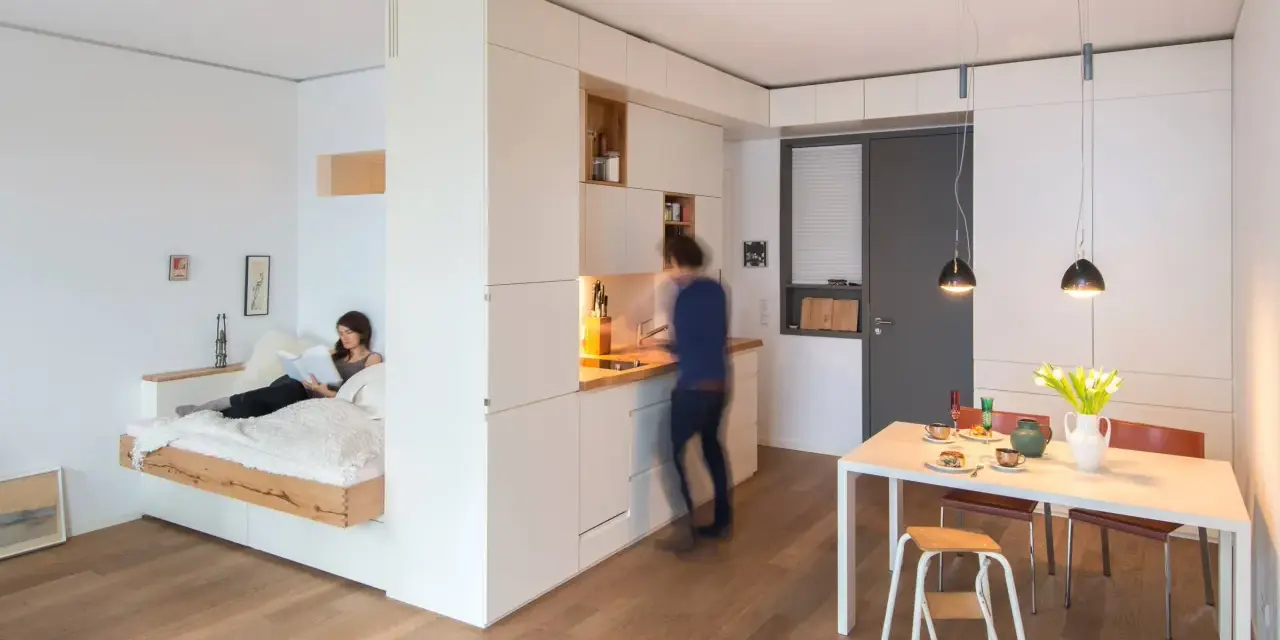 Clevere raumaufteilung ideen: Ein Bettbereich ist vom Wohnbereich durch eine weiße Wand getrennt. Eine Küche und ein Essbereich sind integriert.