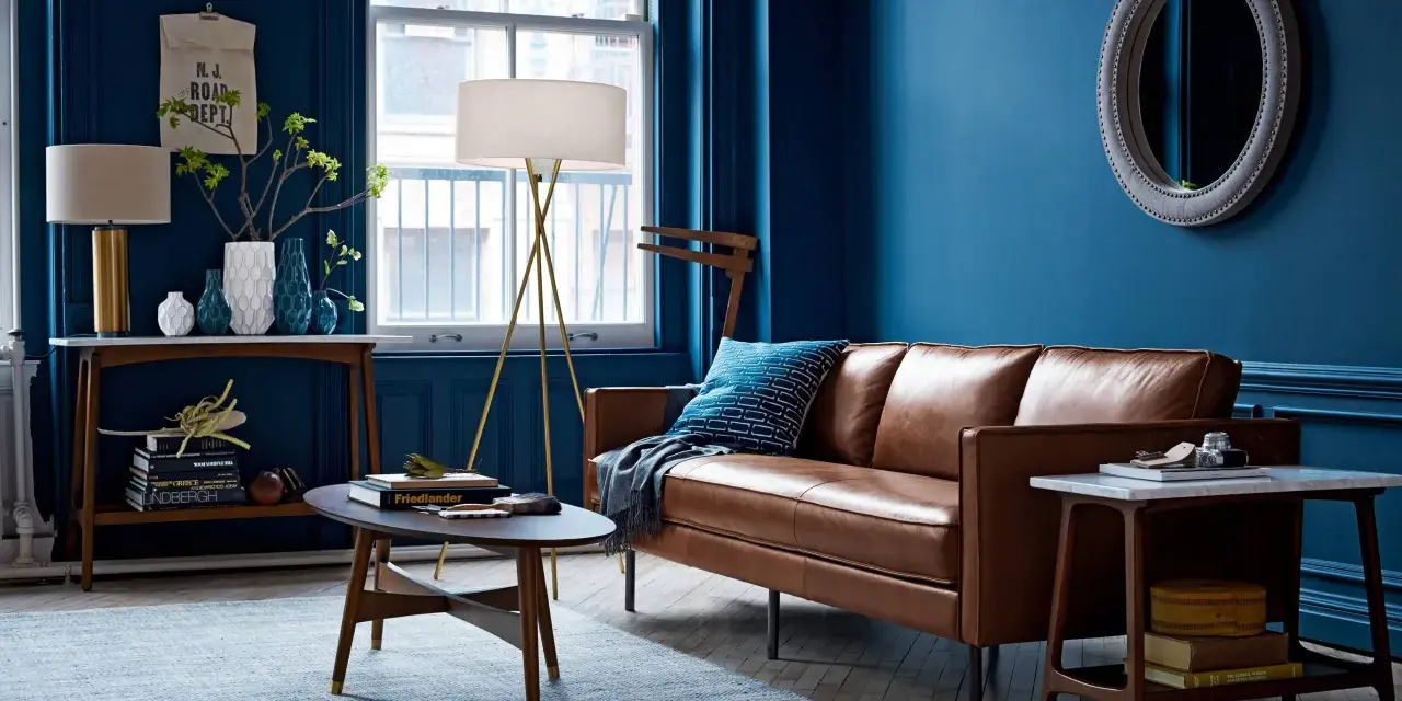 Ein Wohnzimmer mit braunem Ledersofa und blauen Wänden. Das Braun ist die perfekte gegenfarbe von braun, die dem Raum Tiefe verleiht.