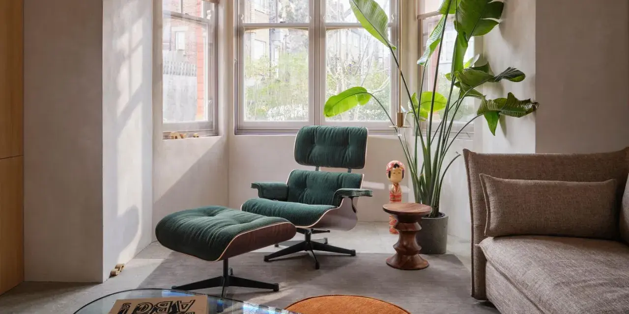 Gemütliches mid century wohnzimmer mit einem dunkelgrünen Sessel und Hocker, einer großen Zimmerpflanze und einem beigefarbenen Sofa.