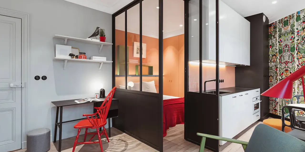 Clever 35 qm wohnung einrichten: Schlafbereich, Küche und Arbeitsplatz sind durch Glaswände getrennt. Bunte Akzente wie der rote Stuhl und die Tapete beleben den Raum.