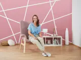 Frau sitzt vor einer rosa Wand mit weißem geometrischem Muster. Tolle Ideen zum Wand streichen und Muster abkleben!