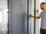 Mann mit Kopfhörern betätigt den Türöffner an der modernen zuwegung haus.