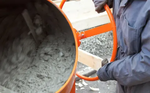 Eine Betonmischmaschine rührt den feuchten Mörtel, der zeigt, aus was Beton besteht: Zement, Wasser und Zuschlagstoffe.