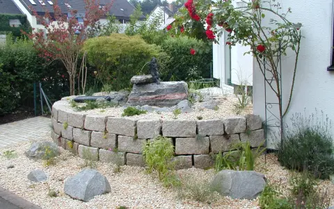 Moderner Hauseingang mit einem geschwungenen Steingarten und einem kleinen Wasserspiel. Ein Hingucker, der zeigt, wie man den Vorgarten modern gestalten kann.