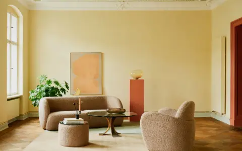 Ein Wohnzimmer mit gelben Wänden und einer grünen Decke, die frisch gestrichen wurde. Gemütliche Bouclé-Möbel und ein runder Couchtisch laden zum Verweilen ein.