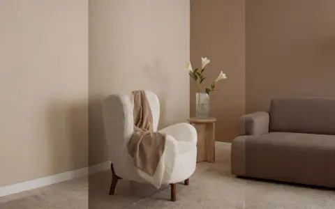 Gemütliches Wohnzimmer mit einem weißen Teddy-Sessel, einer braunen Couch und einer Vase mit Lilien. Warme Farben dominieren die Szene.