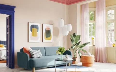 Ein Wohnzimmer mit hellrosa Decke und Wand, blauem Sofa, bunten Bildern und einem Durchgang zu einem Schlafzimmer.