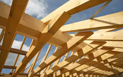 Holzkonstruktion eines Dachstuhls im Bau, mit sichtbaren Balken und Streben. Das Sprengwerk des Dachstuhls wird durch das Sonnenlicht beleuchtet.