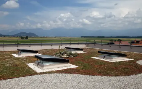 Grünes Flachdach mit leichter Neigung, vier Dachfenstern und Blick auf Berge.