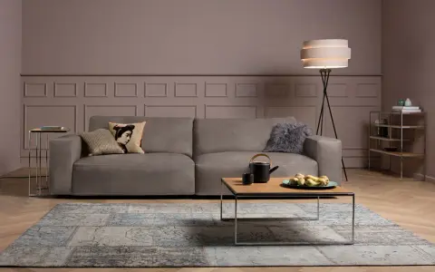 Ein taupefarbenes Sofa mit Kissen und ein Couchtisch mit Obst. Die Wandfarbe ist ein warmes Braun, das zeigt, welche Farbe passt zu Taupe.