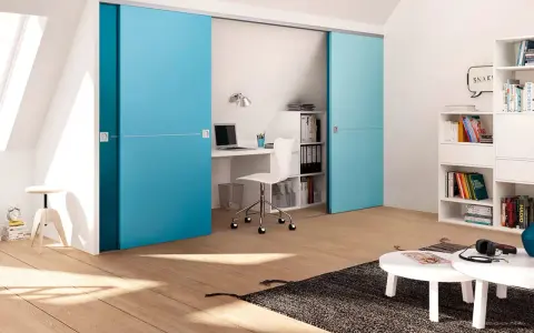 Ein kleines Arbeitszimmer einrichten: Blaue Schiebetüren verbergen einen Schreibtisch mit Laptop und Bürostuhl. Bücherregale und ein Couchtisch ergänzen den Raum.