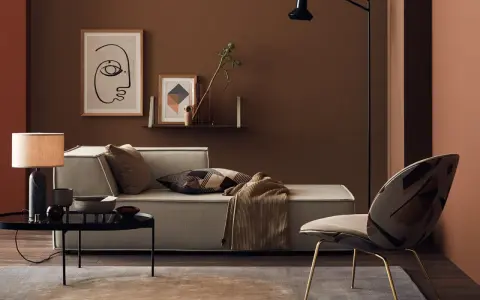 Gemütliches Wohnzimmer mit Sofa, Sessel und Tisch. Die Wände sind in warmen Brauntönen gehalten, die sich mit den Textilien und Dekorationen **braun mischen**.